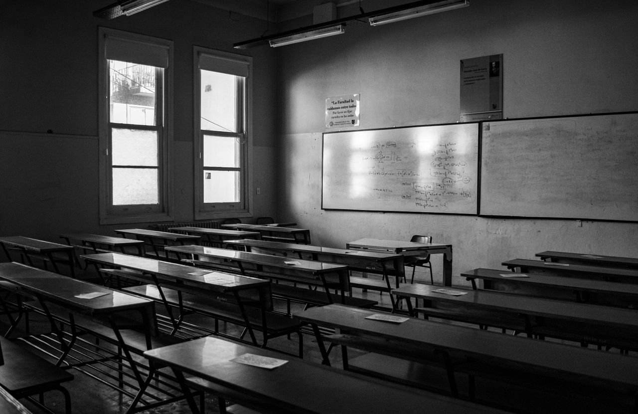 A black and white photo of an empty classroom with desks and chalkboards.